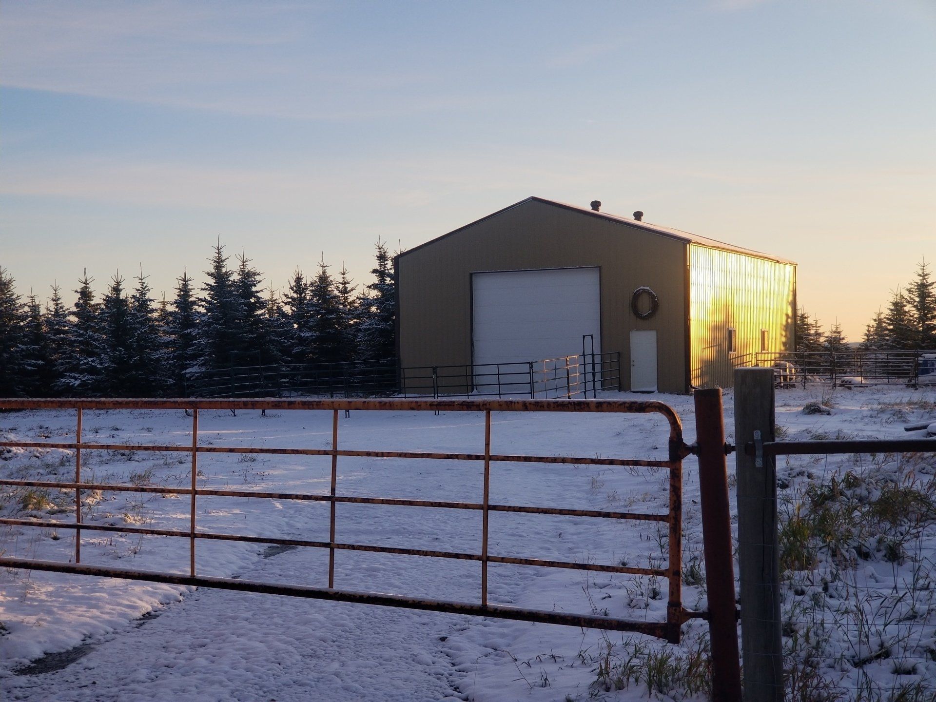 A barn is behind a fence with snow on the ground