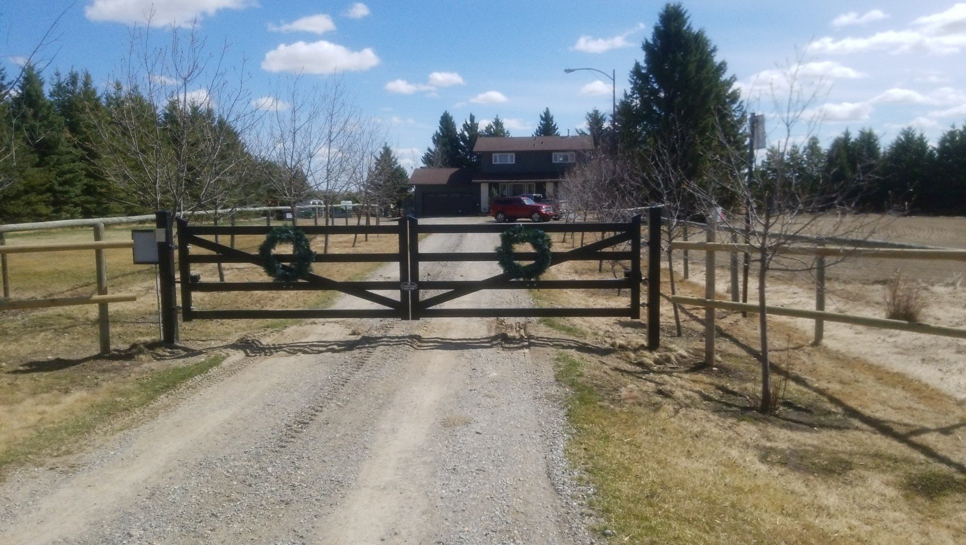 A dirt road with a fence and a gate leading to a house.