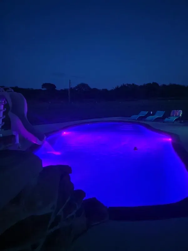 A swimming pool is lit up with purple lights at night.