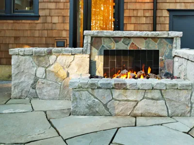 A stone fireplace is sitting on a patio in front of a house.