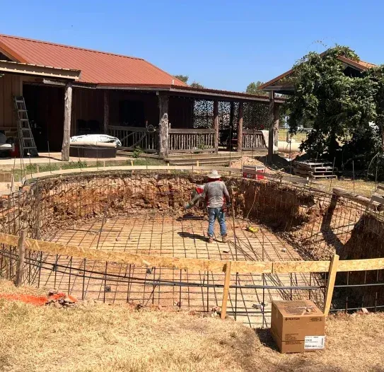 A man is standing in front of a swimming pool under construction.