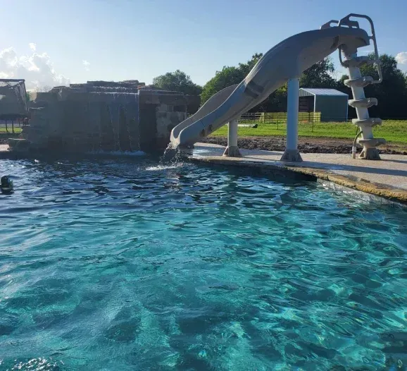 A person is swimming in a pool with a water slide in the background