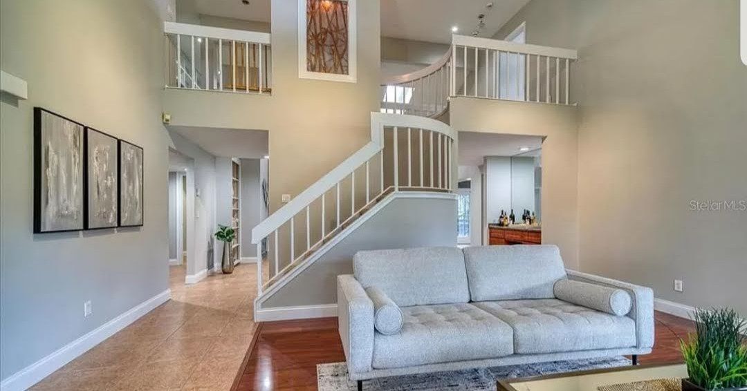 Living room with a white sofa, staircase, and artwork on the walls. Living room with a white sofa, staircase, and artwork on the walls.