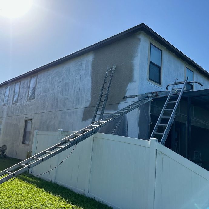 Ladders leaning against a two-story house being repaired, with patches of new stucco on the exterior wall. Ladders leaning against a two-story house being repaired, with patches of new stucco on the exterior wall.