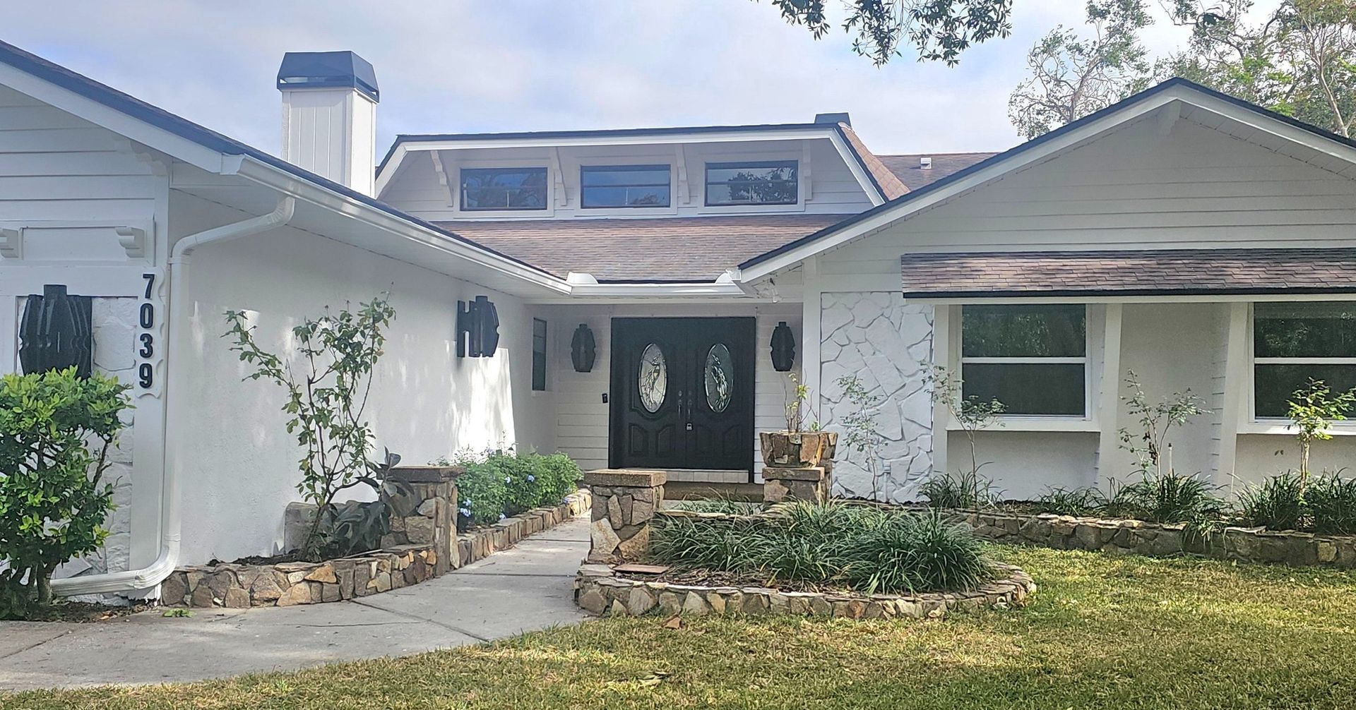 White stucco house with dark door, stone accents, and small front yard. White stucco house with dark door, stone accents, and small front yard.