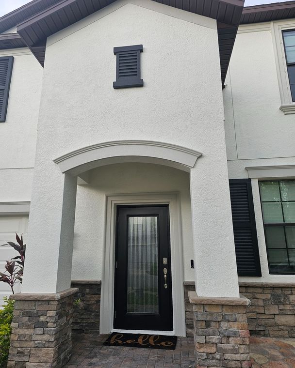 White stucco house with black door, shutters, and stone base. White stucco house with black door, shutters, and stone base.