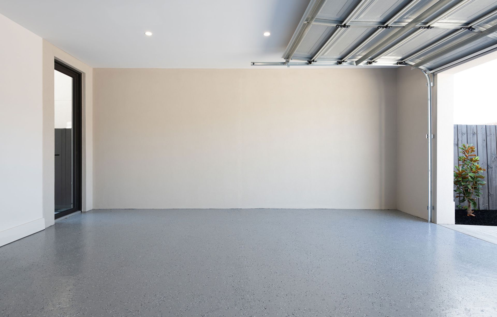Empty garage with gray epoxy floor and beige walls. Open garage door on right. Empty garage with gray epoxy floor and beige walls. Open garage door on right.