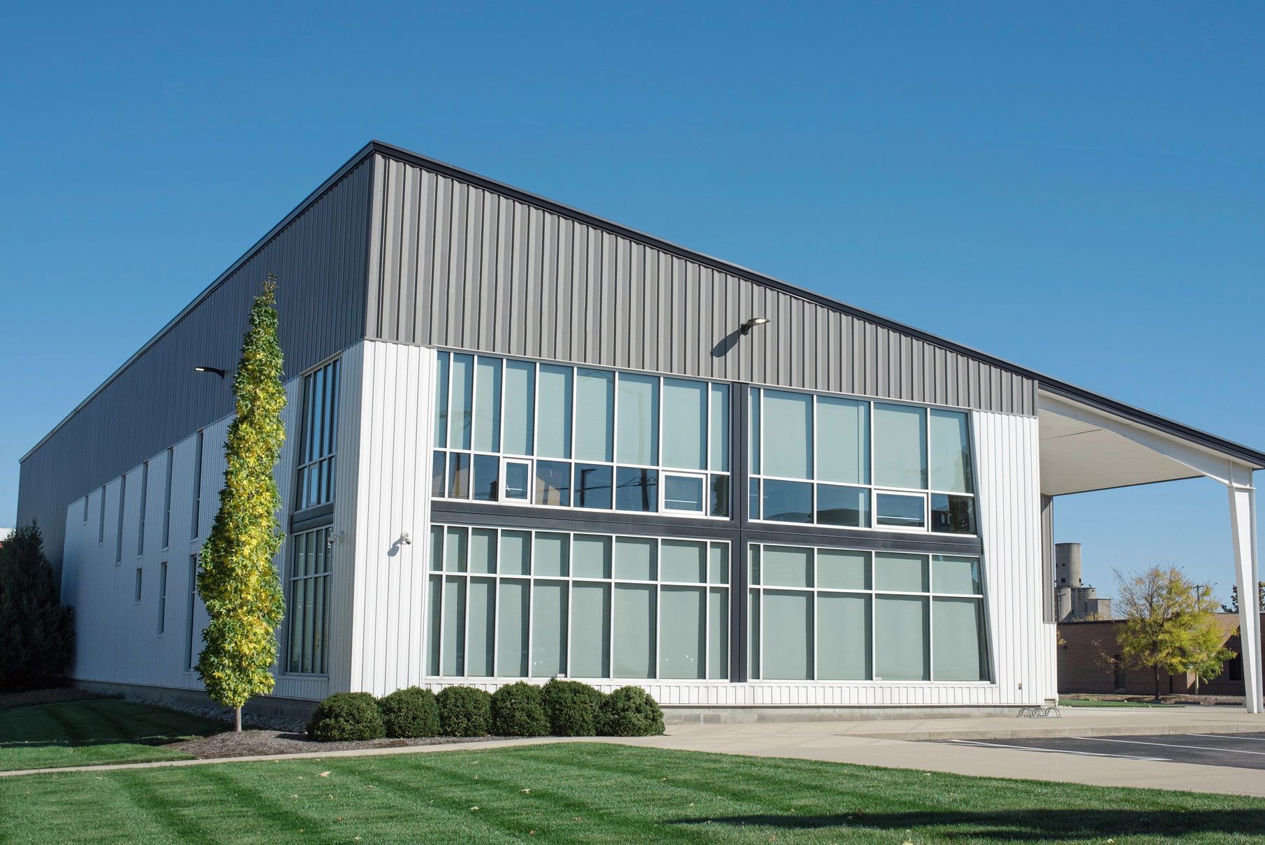 Modern building with a sloped metal roof and large windows, set on a green lawn under a blue sky. Modern building with a sloped metal roof and large windows, set on a green lawn under a blue sky.