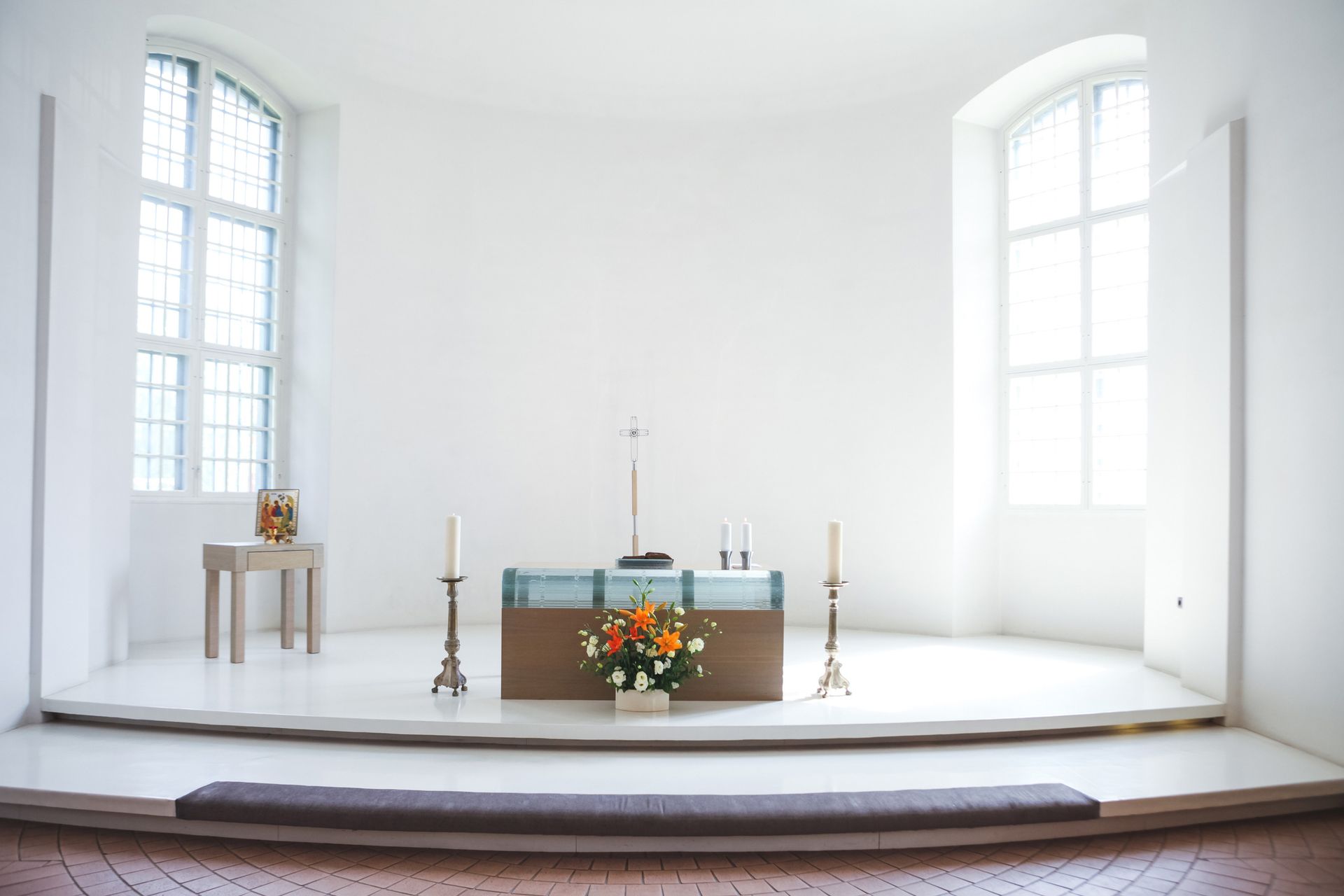 Bright, white sanctuary with an altar, two windows, flowers, and candles. Bright, white sanctuary with an altar, two windows, flowers, and candles.