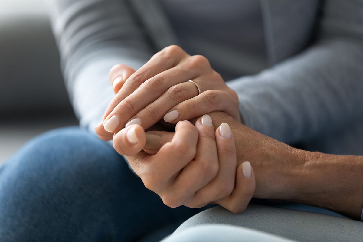 A woman is holding another woman 's hand while sitting on a couch.