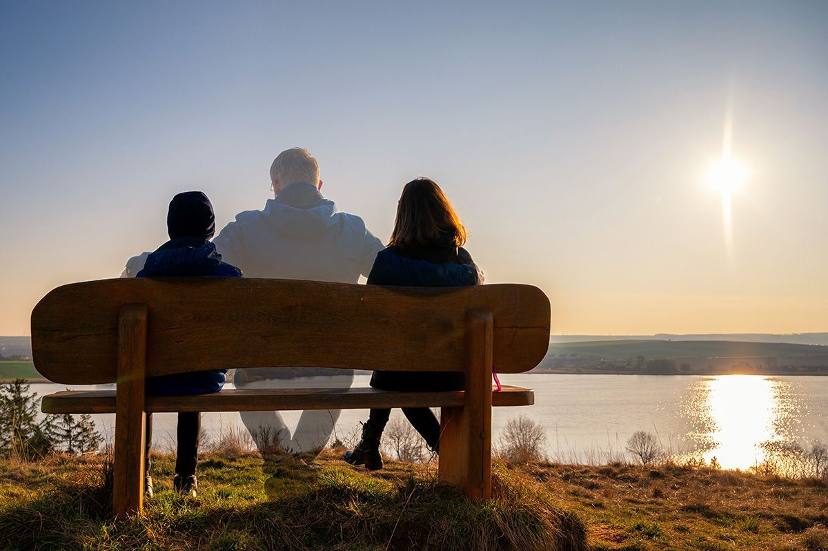 A man and a woman are sitting on a bench overlooking a lake.