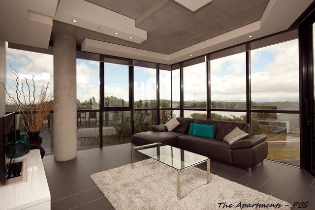 Modern living room with floor-to-ceiling windows, brown leather sectional, glass coffee table, and gray tiled floor. — Rectified Edge Tiling & Bathroom Renovations in Fyshwick, ACT