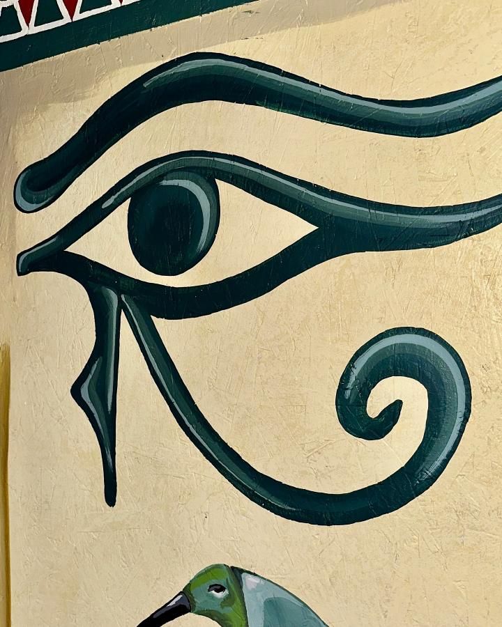 Eye of Horus symbol in teal on a yellow background.