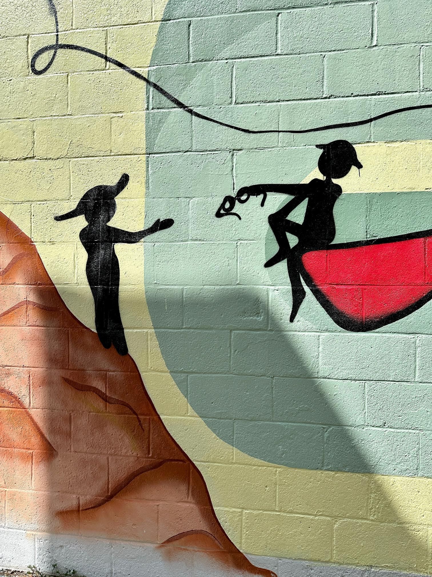 Mural: Silhouetted figures on brick wall, one reaching, other seated on red shape, line connecting them.