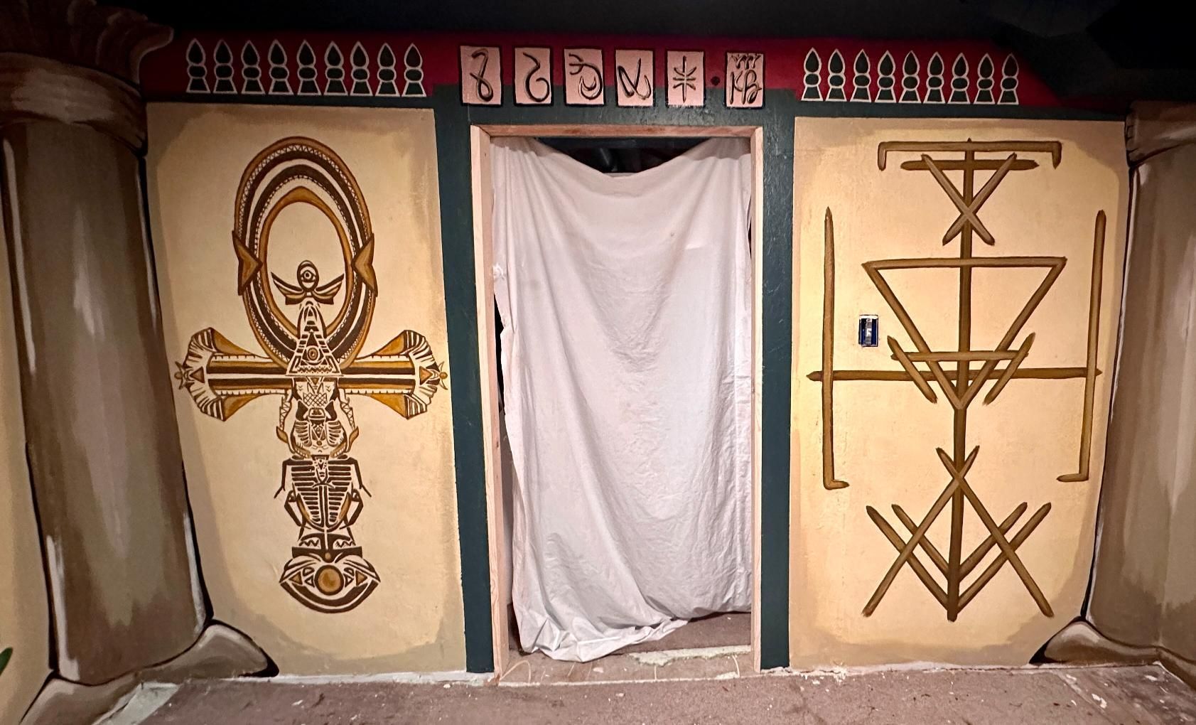 An Egyptian-themed room with hieroglyphics. Ankh symbol on the left wall, a geometric design on the right.