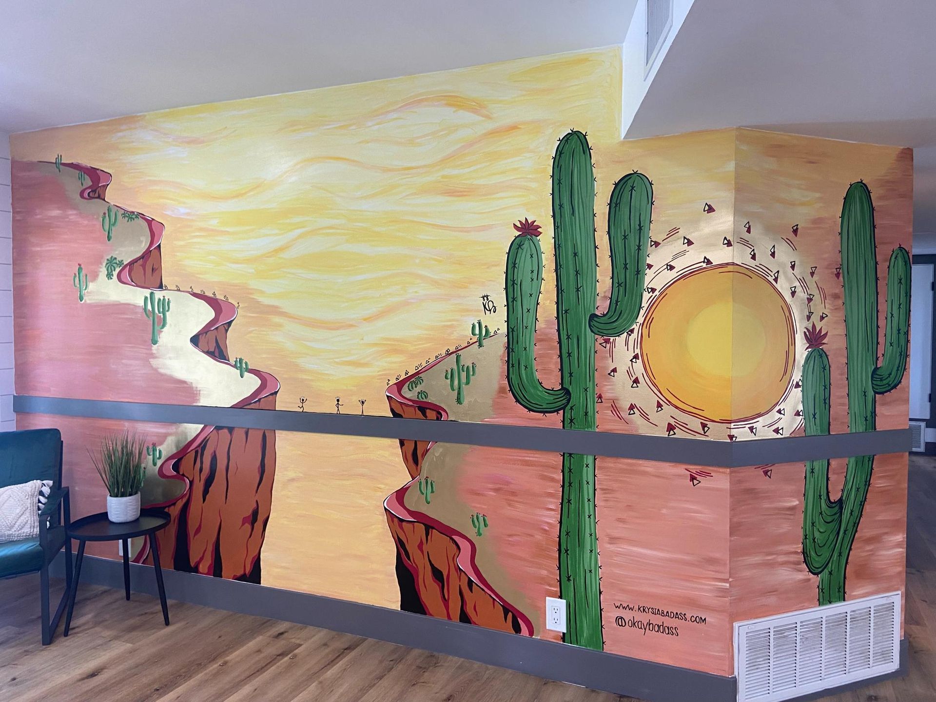 Mural of a desert landscape with a winding path, cacti, and setting sun on a textured, colorful wall.