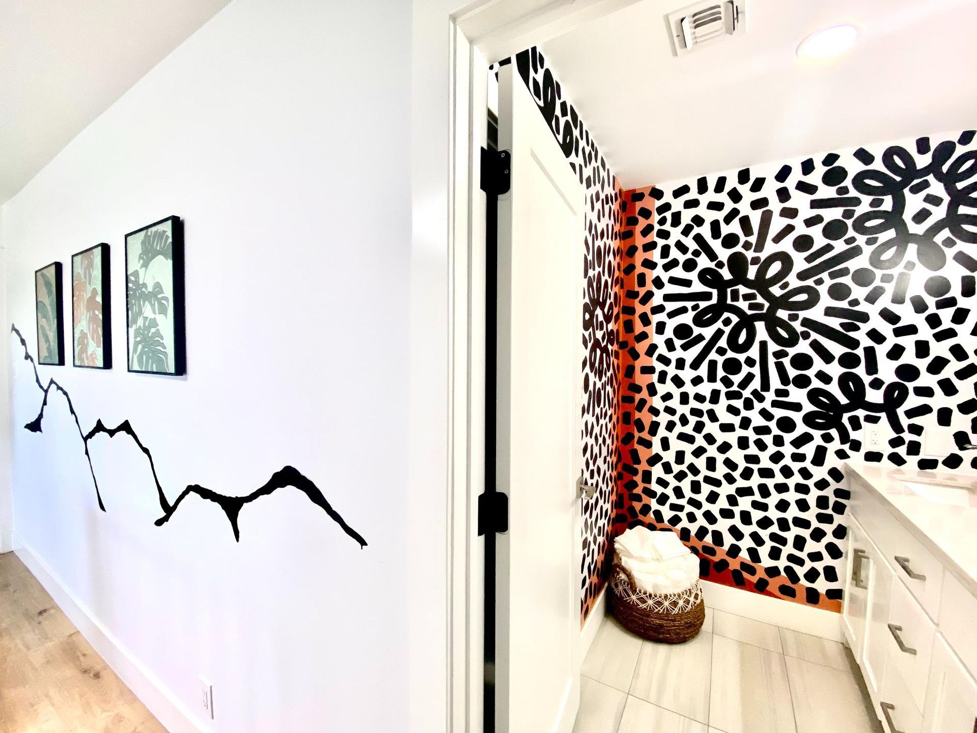 Hallway with black and white patterned bathroom entrance, white walls, art, and black mountain outline.