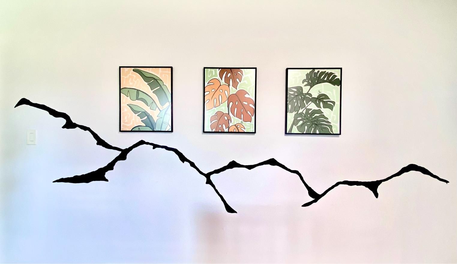 Three framed botanical prints above a black, branch-like wall decoration on a white wall.