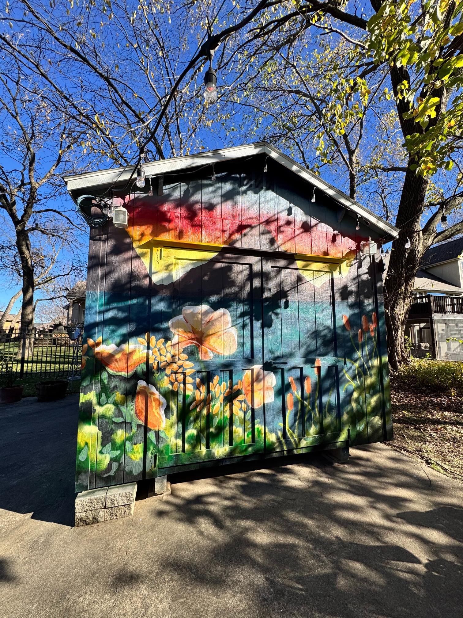 Colorful mural of flowers and sunset on a wooden shed in a park.