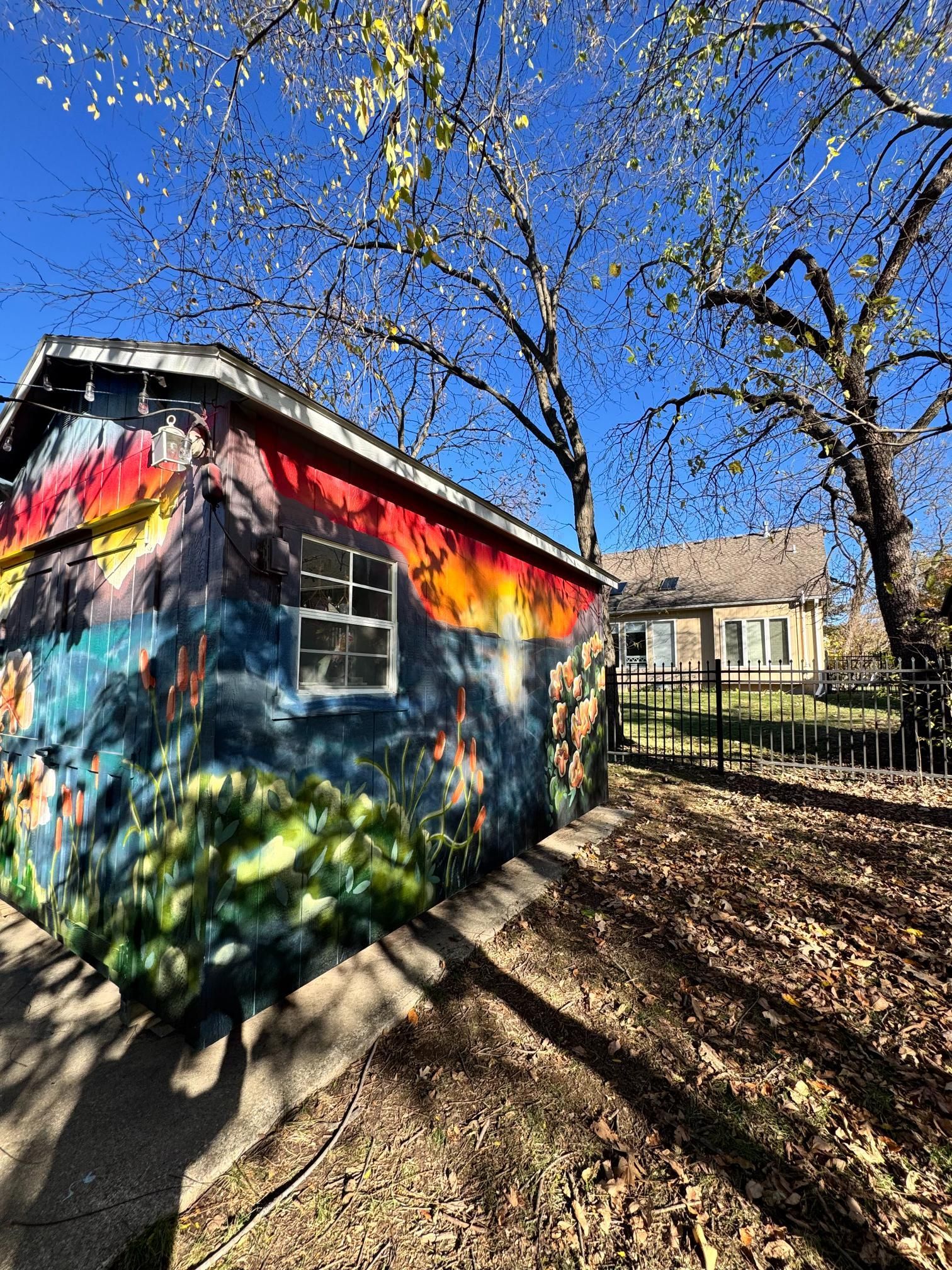 Colorful mural on a shed, bright sky. Another house in the background.