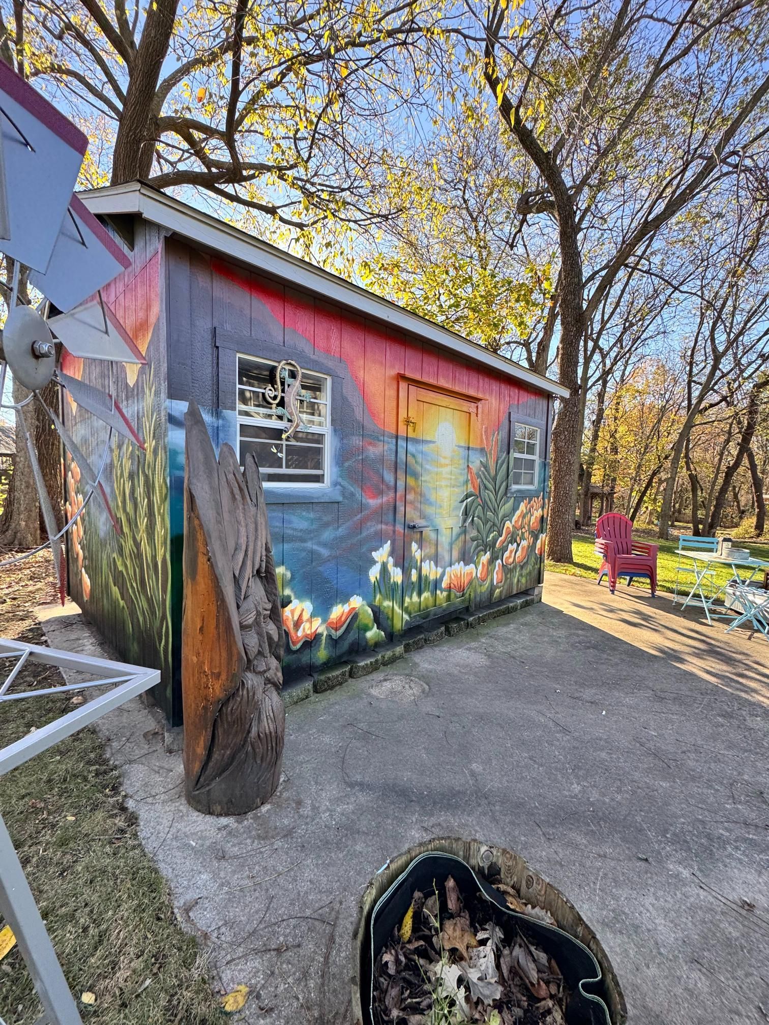 Colorful painted shed with sunset scene; tree and windmill in yard.