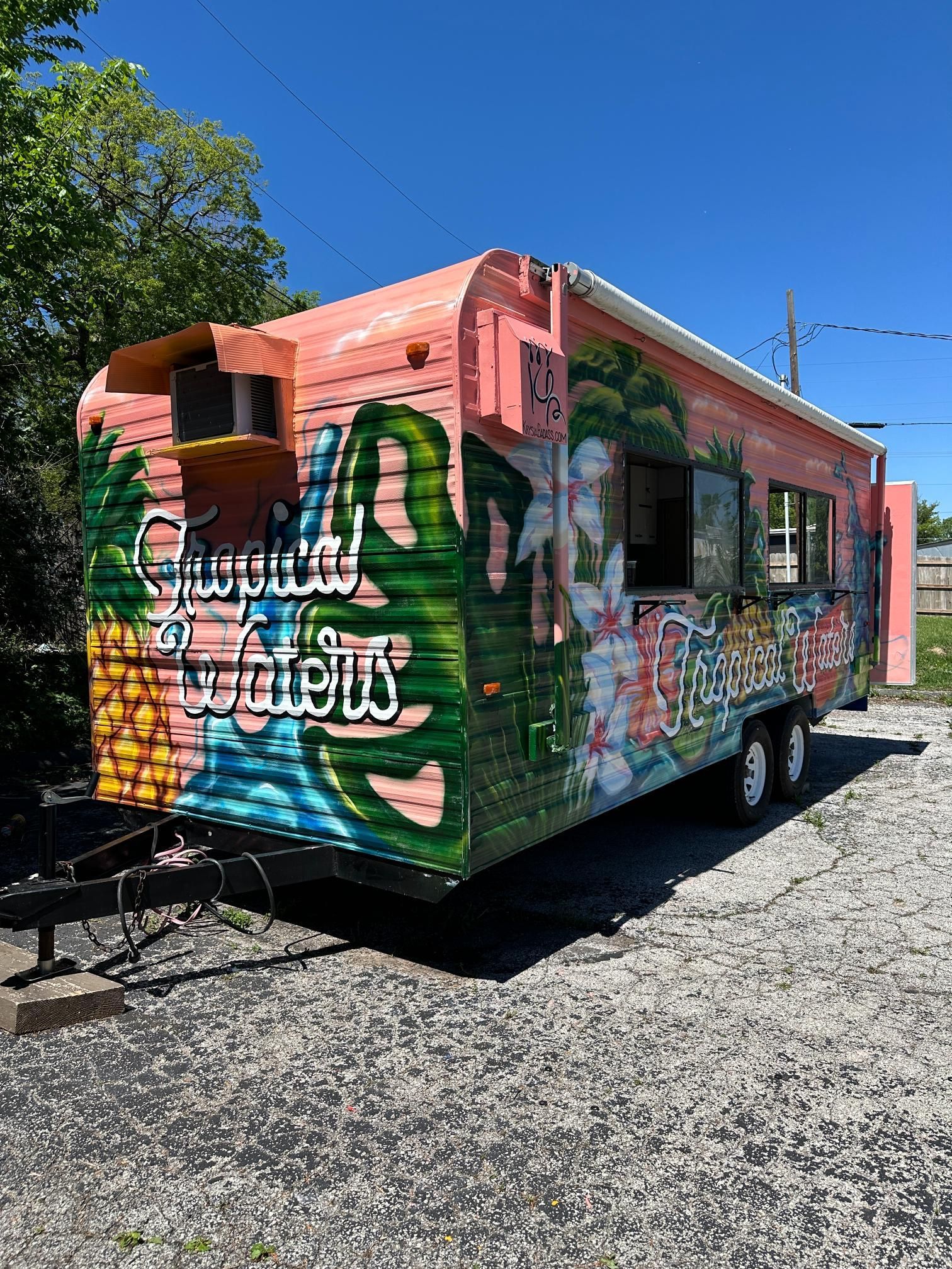 Colorful food truck with tropical mural, parked on a gravel lot under a sunny sky.