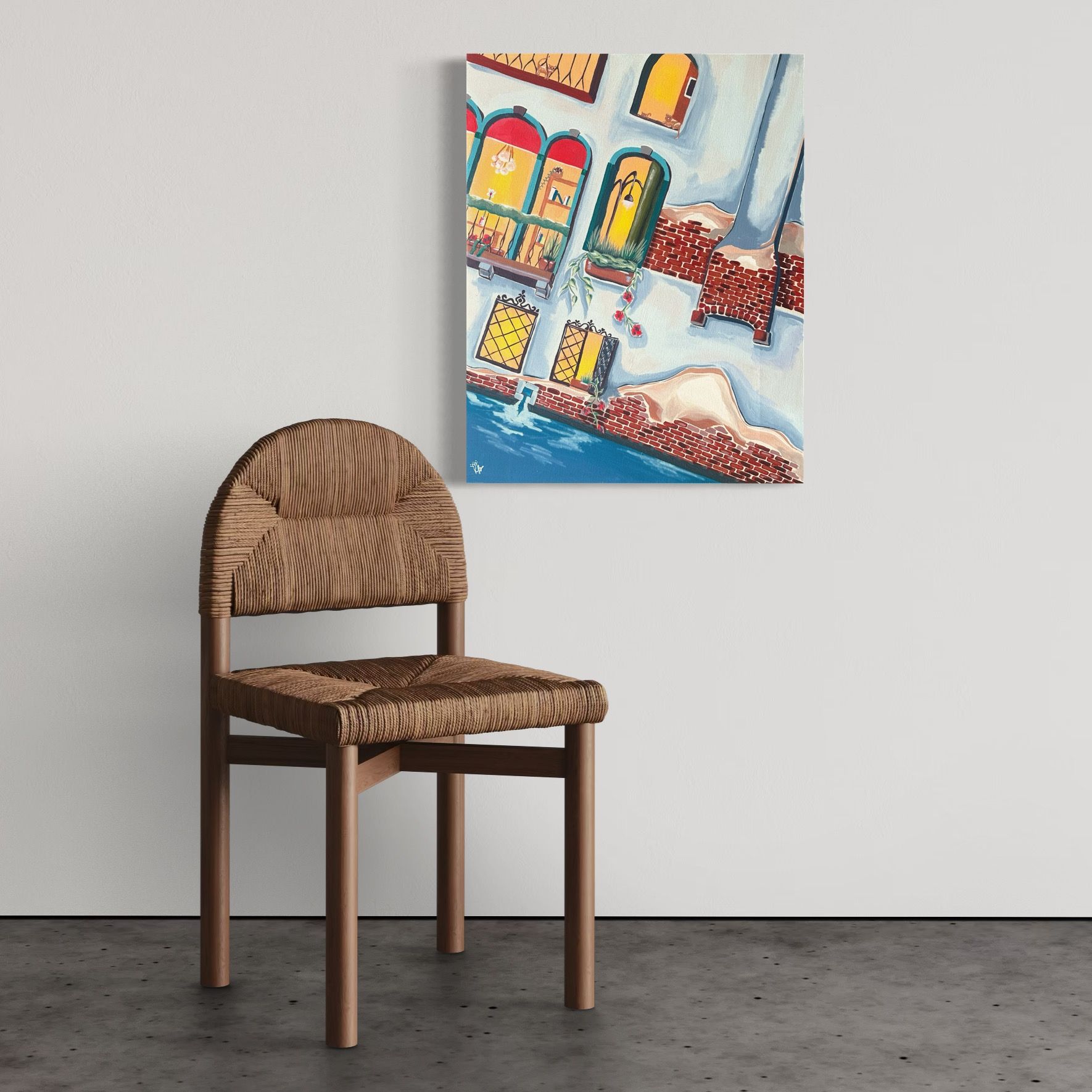 A woven chair stands before a wall with a colorful painting of a building overlooking water.