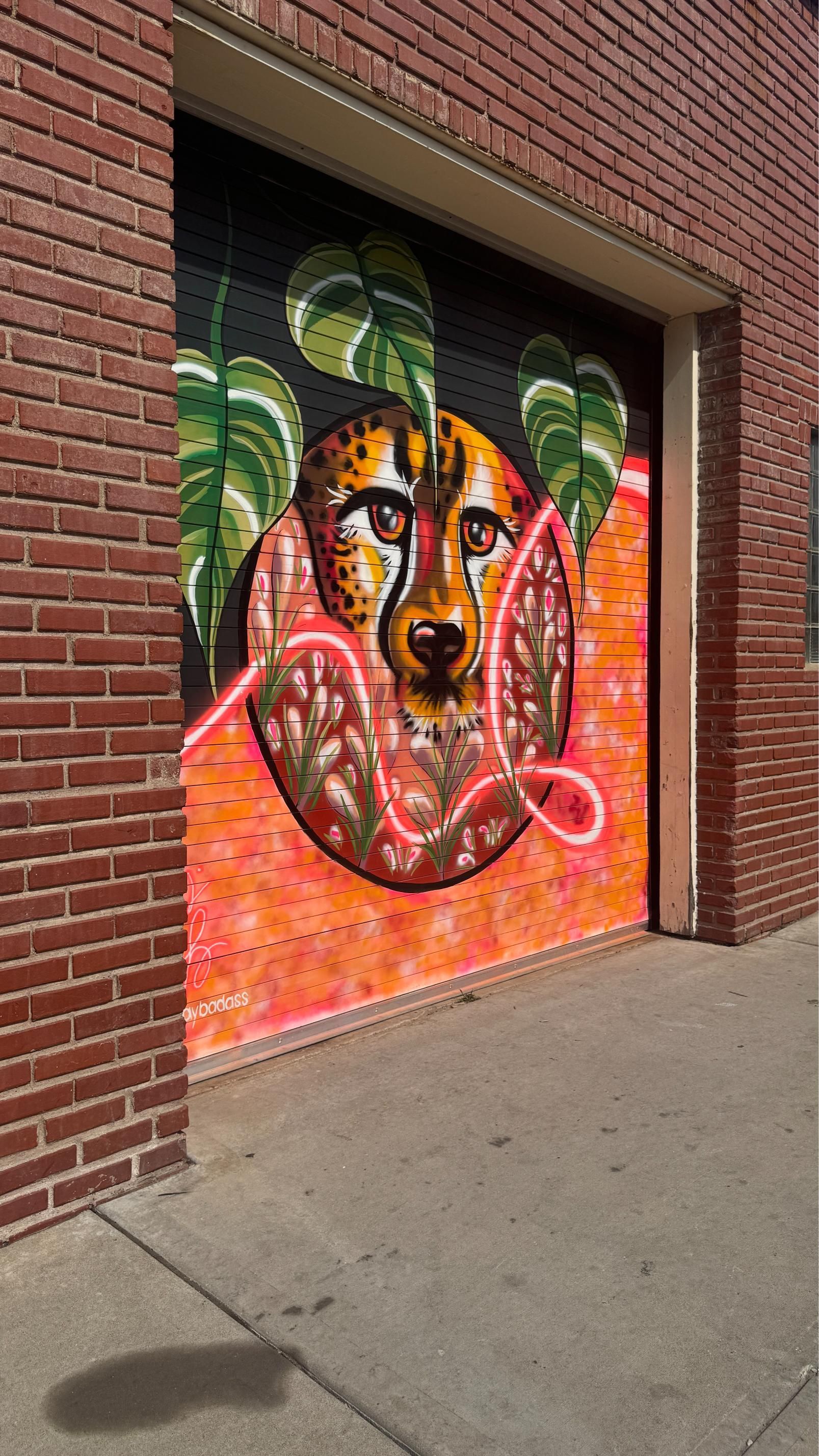 Cheetah mural on a garage door. Orange, brown and green paint. Leaves and neon-like pink line.