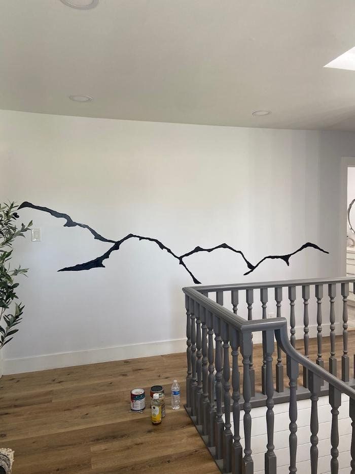 Black mountain range wall art on white wall, adjacent to a gray stair railing and wood floor.