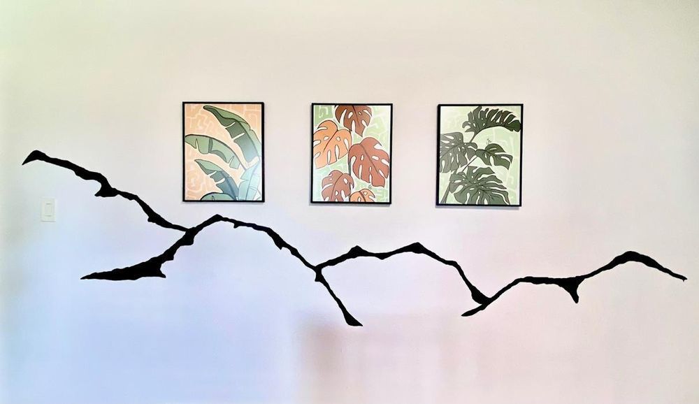 Three framed botanical prints above a black, abstract wall decoration on a pink wall.