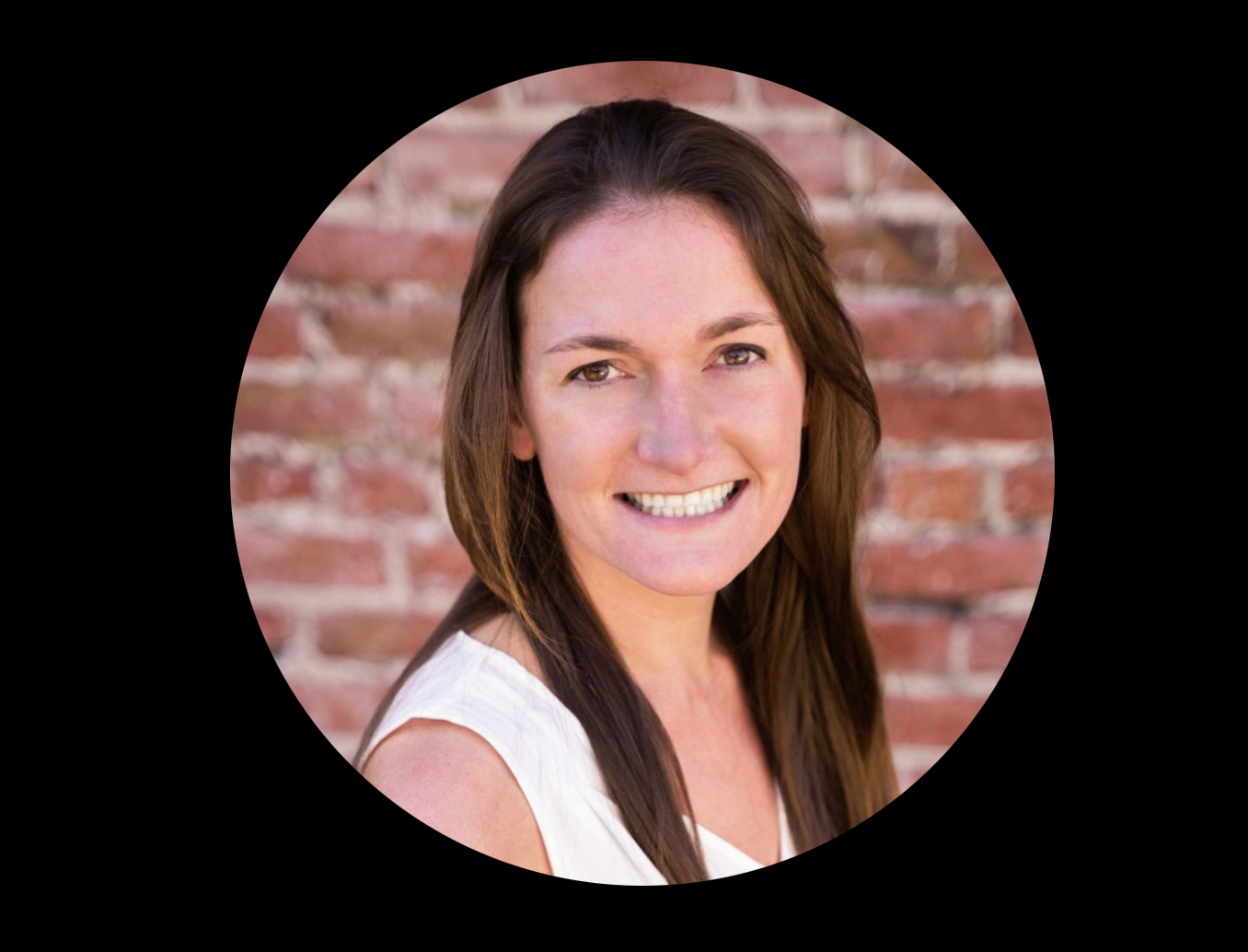Woman with long brown hair smiles in front of a brick wall.