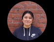 Woman in gray Nike hoodie smiles in front of a brick wall.