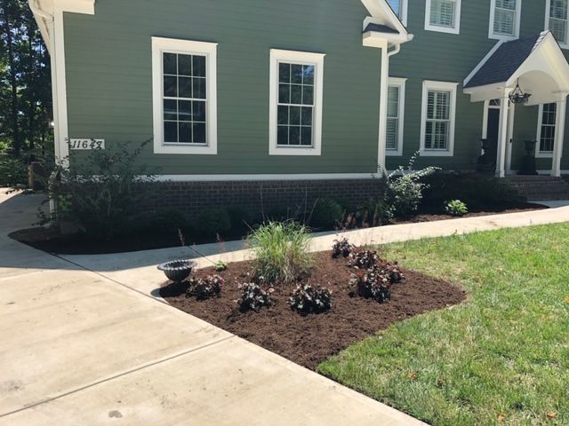 Green house with white trim and a newly mulched garden bed, driveway.