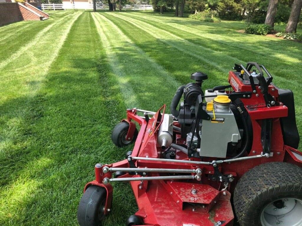Red zero-turn lawn mower cutting striped pattern in green lawn. Sunny day.
