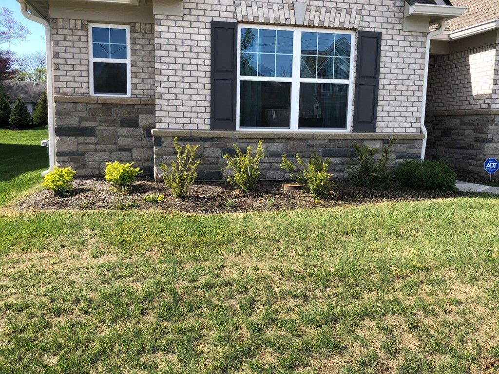 A brick house with a green lawn and landscaping beds.