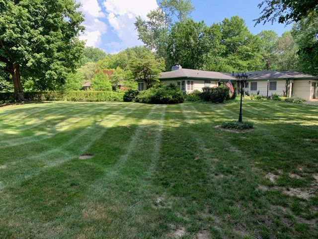 Lawn mowed with striping pattern in front of a single-story house, trees, and a blue sky.