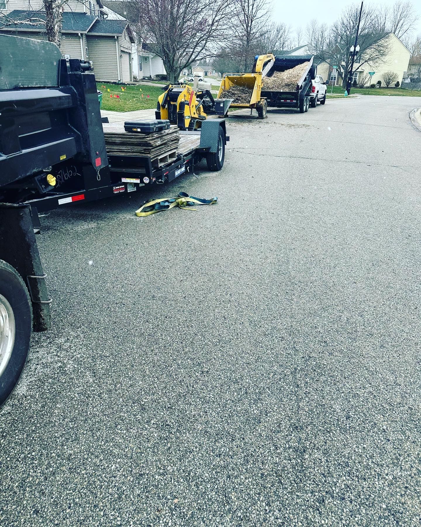 A dump truck, trailer, and excavator on a street loading debris.