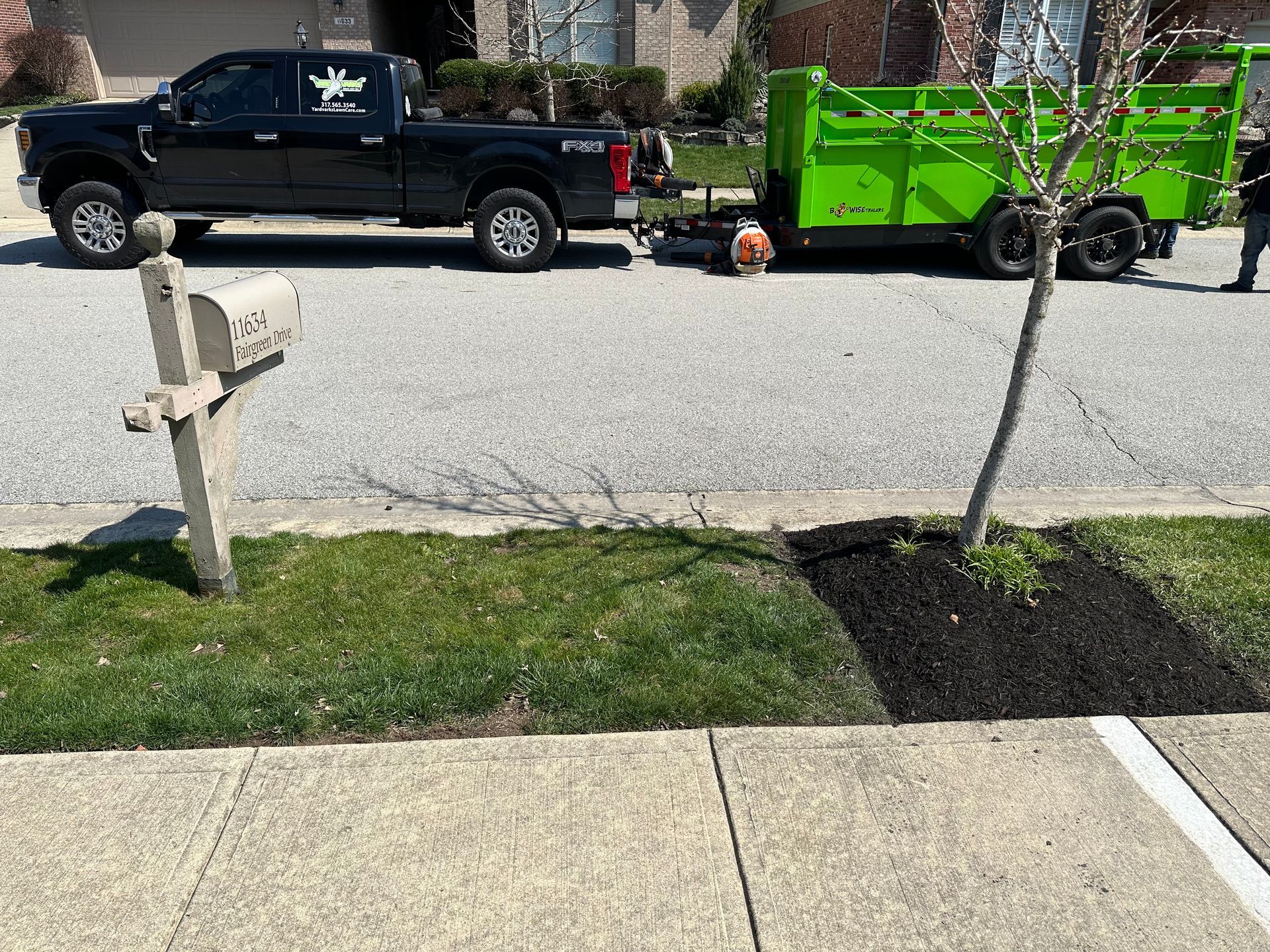 Black truck pulling a green trailer, parked on a street. A mailbox is in the foreground.