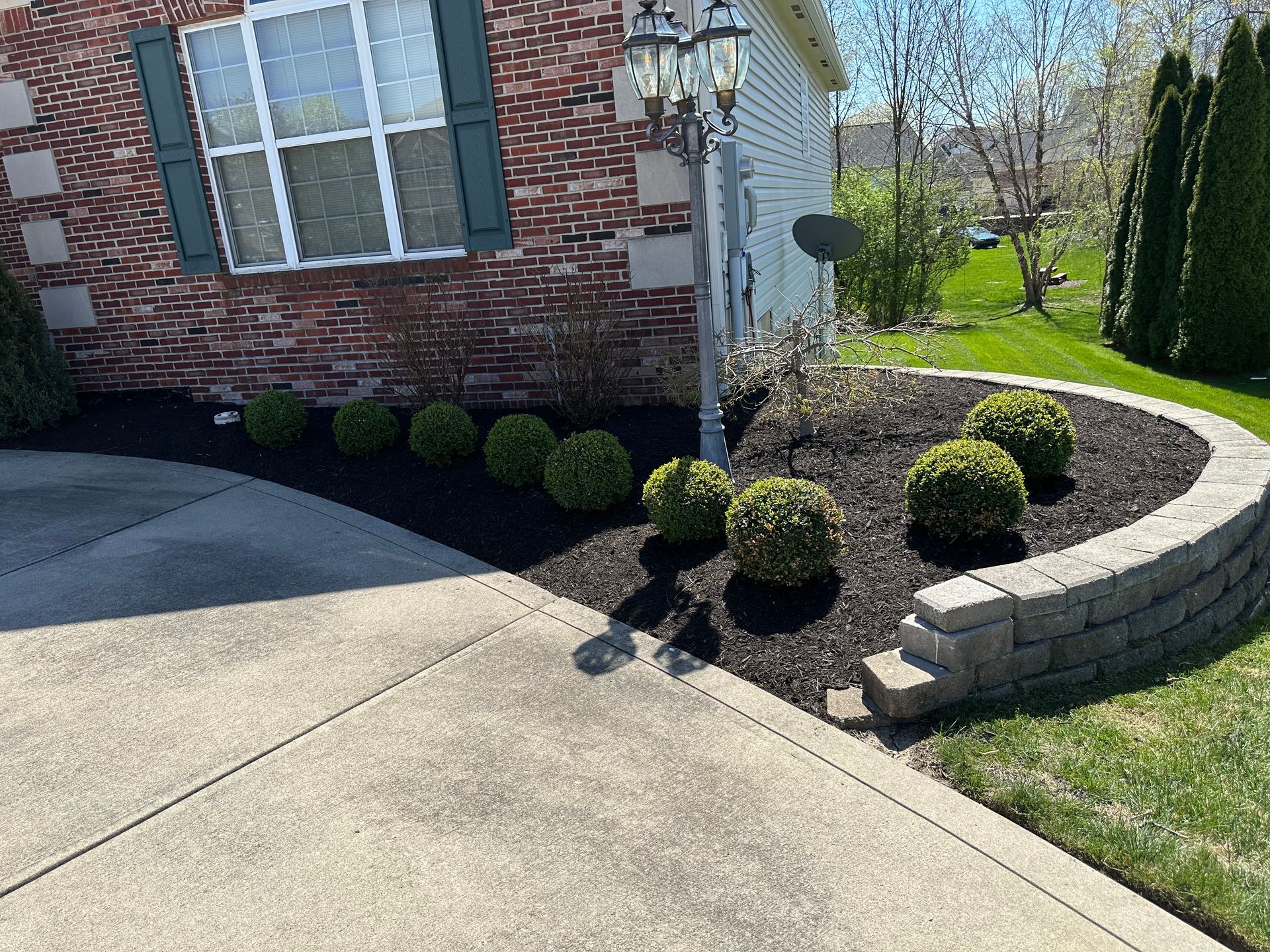 Brick house with driveway and landscaped garden bed with green shrubs and a retaining wall.