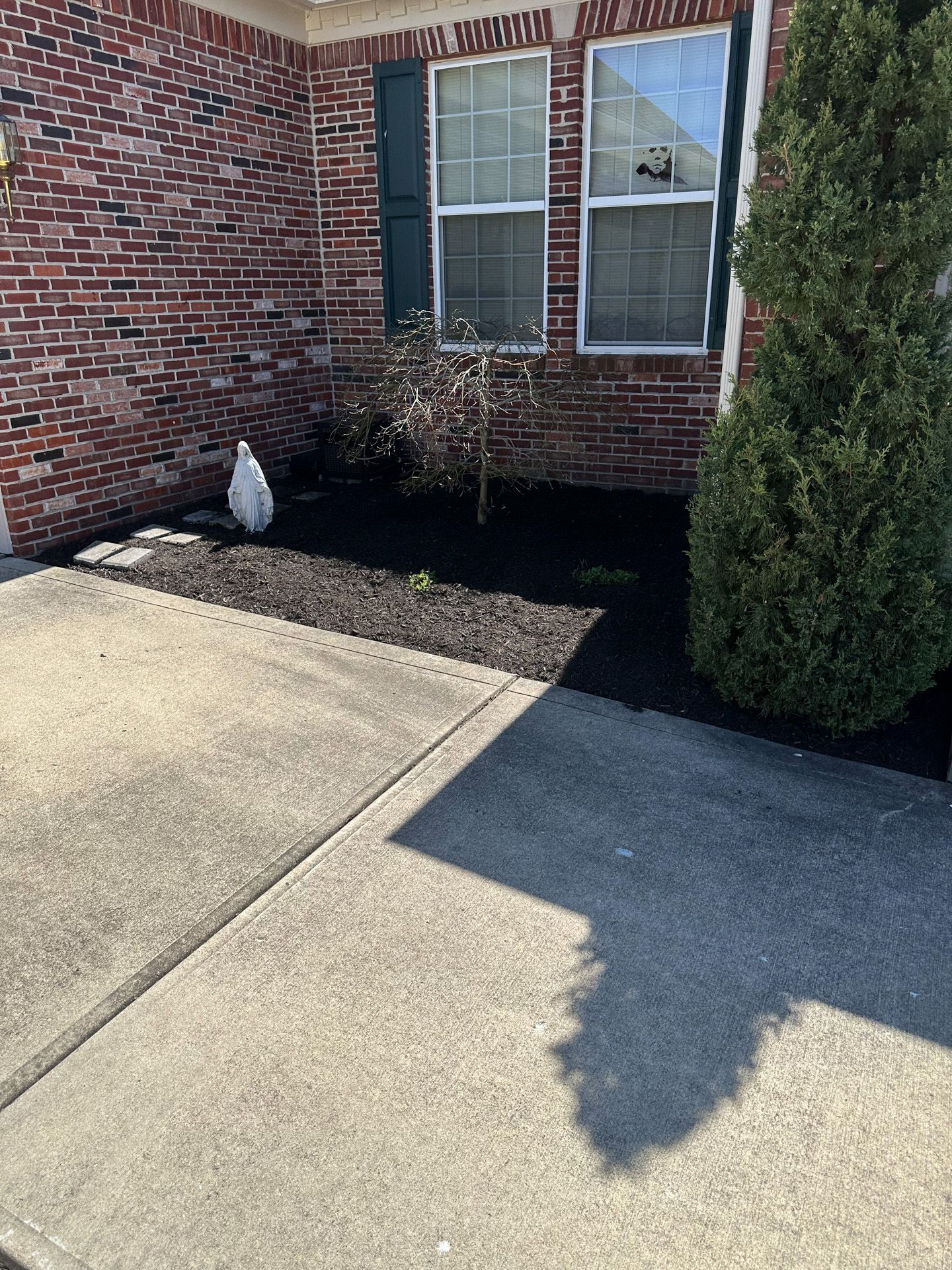 Exterior view of house with brick facade, windows, mulch, and a sidewalk.