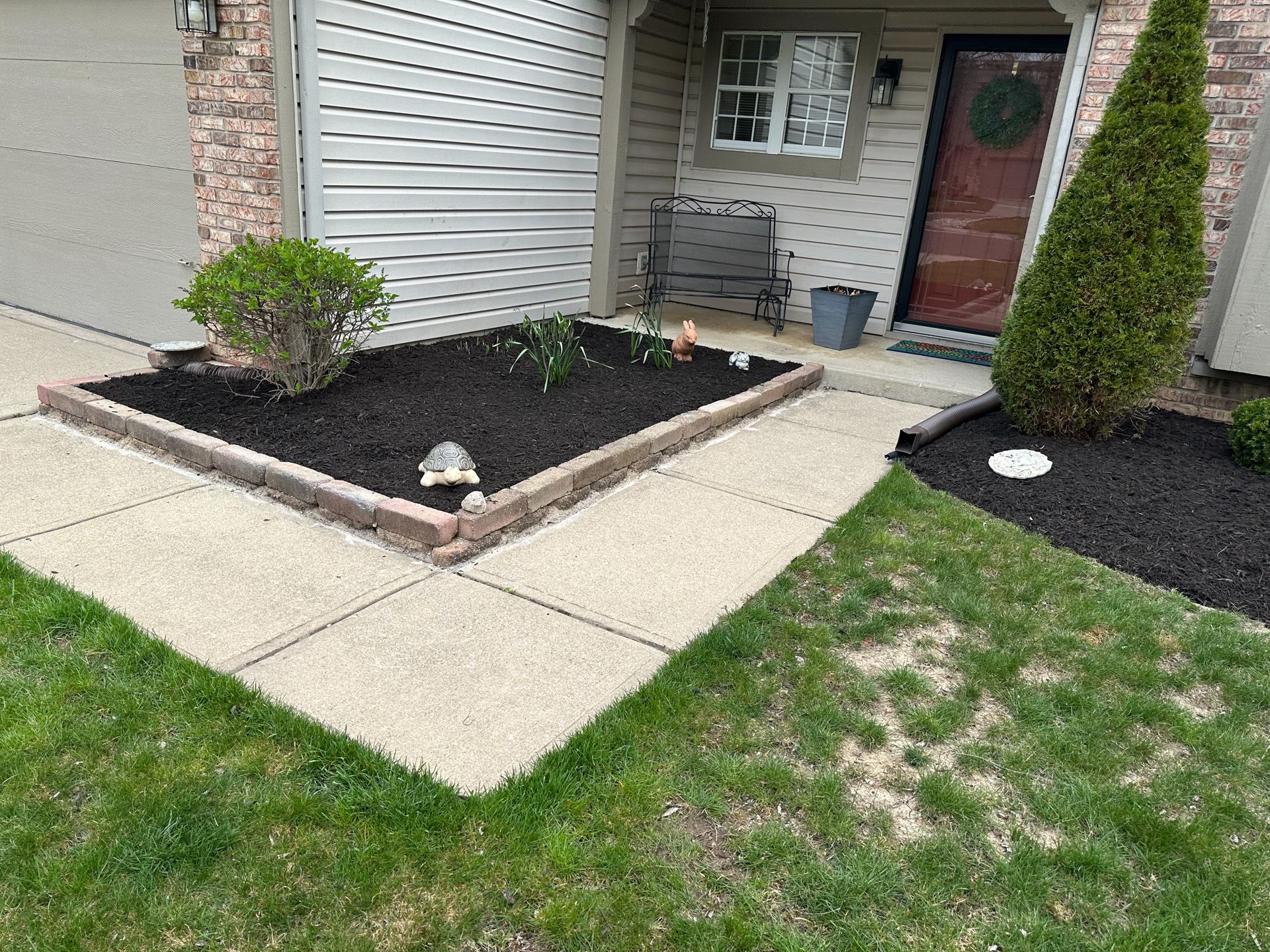 A landscaped front yard with a flower bed, brick edging, and green grass.
