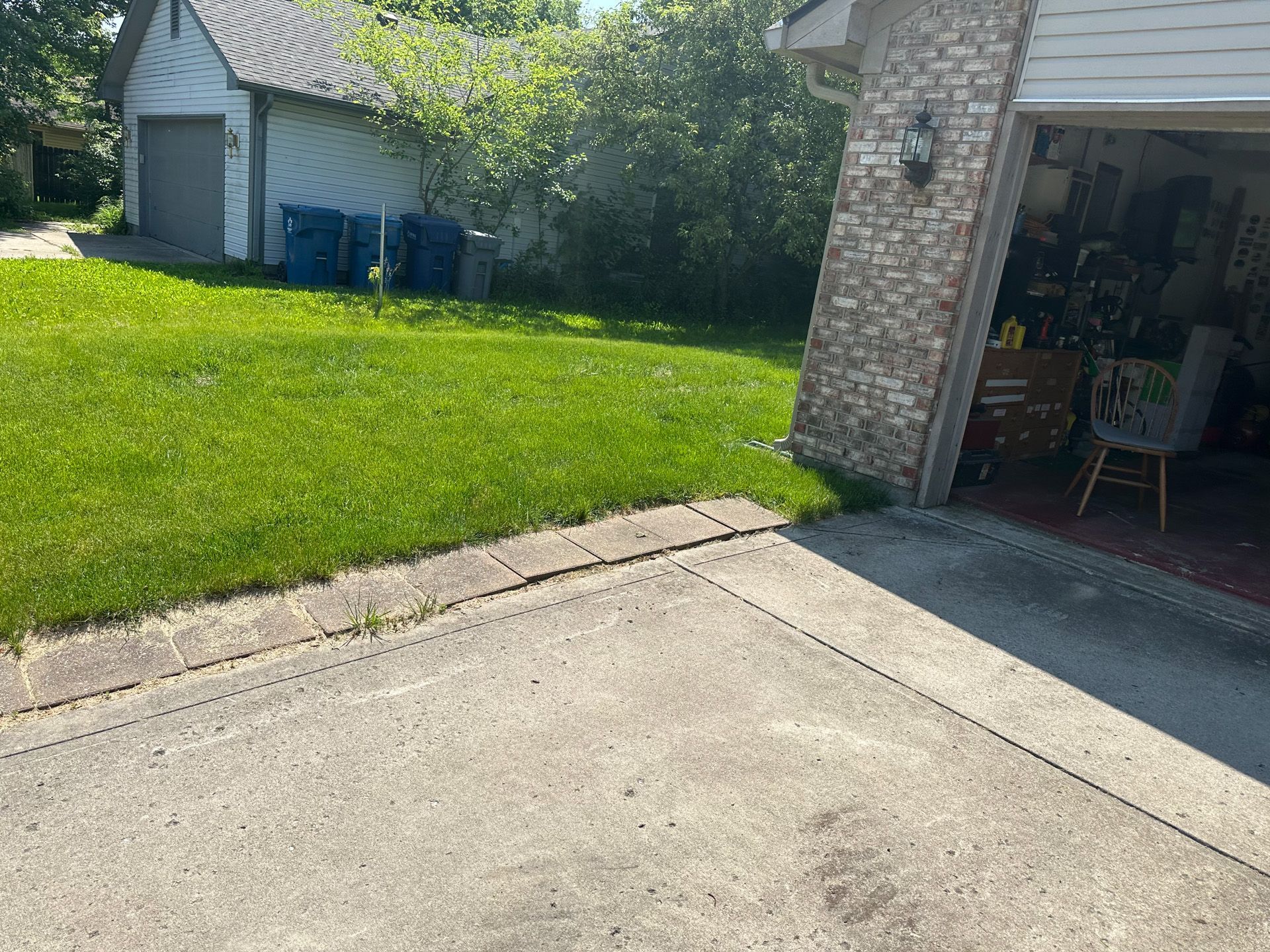 A concrete driveway and grass lawn. A garage sits on the right, and a shed in the distance.