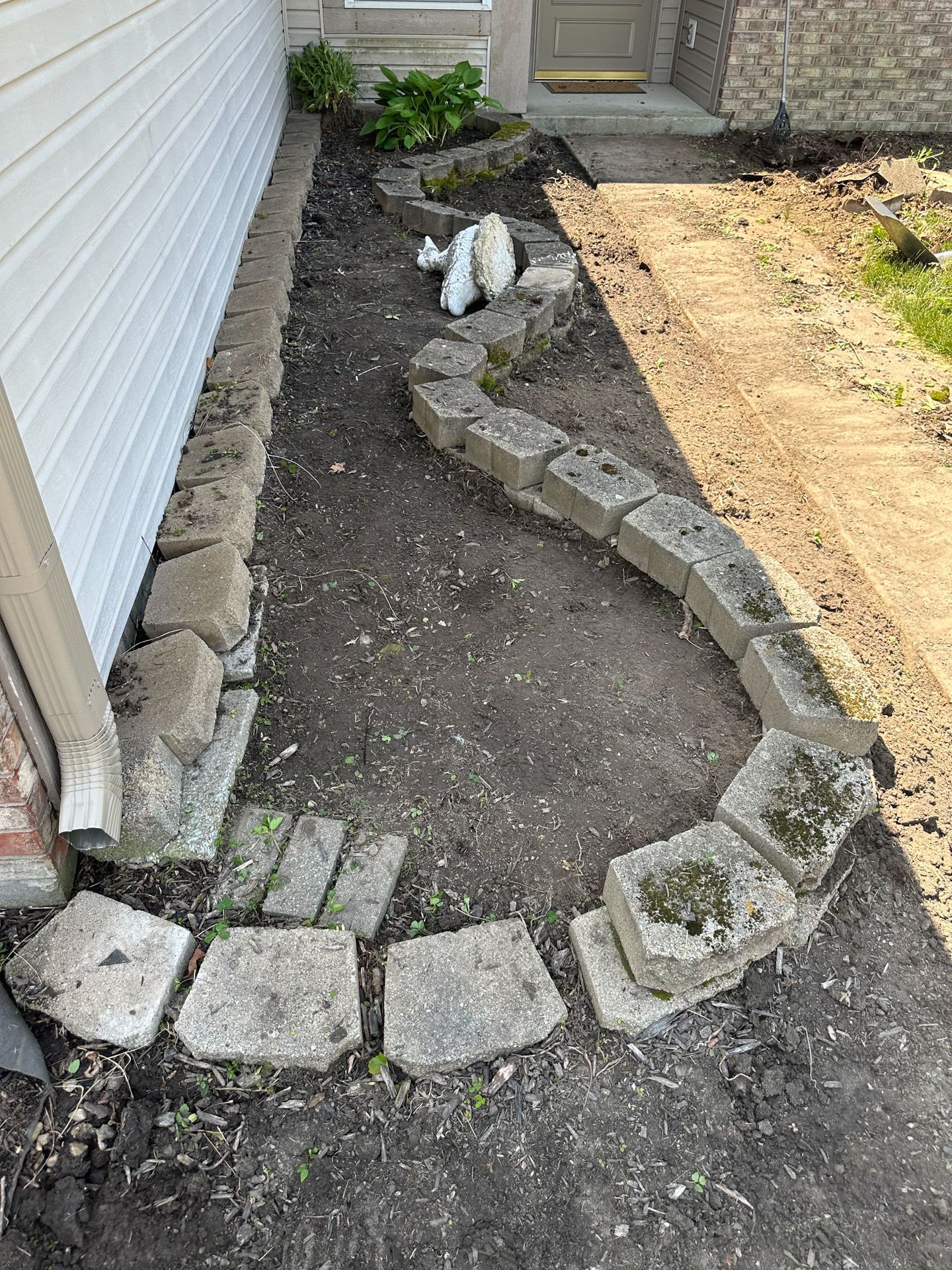 A flower bed with concrete blocks as borders along a house and walkway.