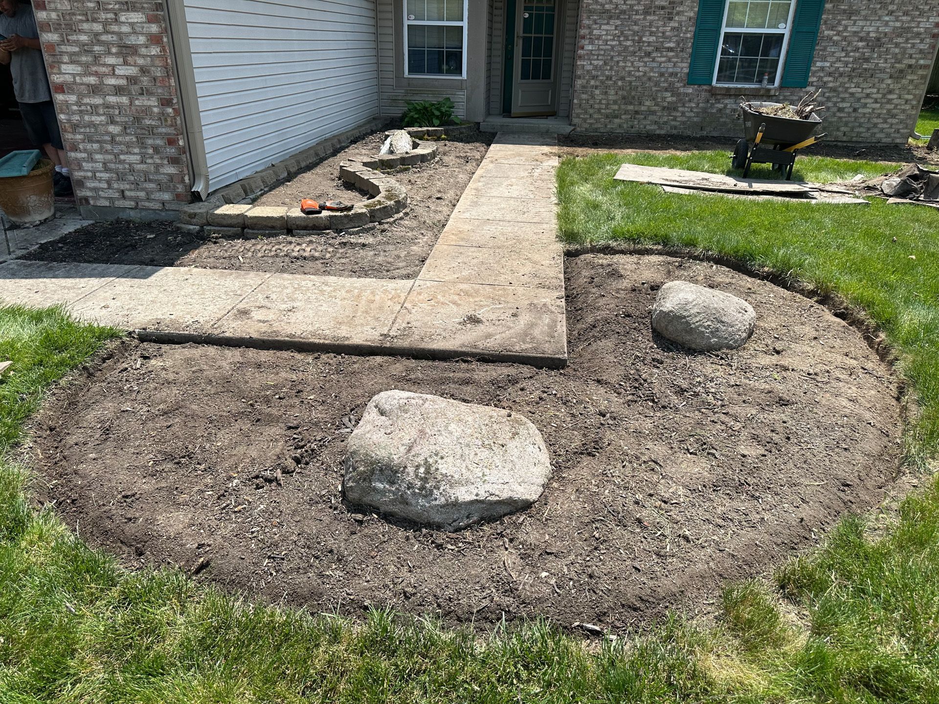 A front yard with a circular flower bed containing two large rocks. A concrete path leads to the front door.
