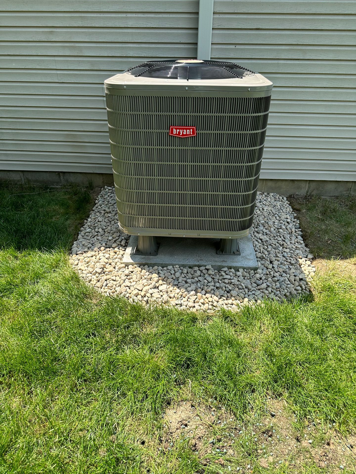 An outdoor air conditioning unit on a gravel pad next to a light-colored house.