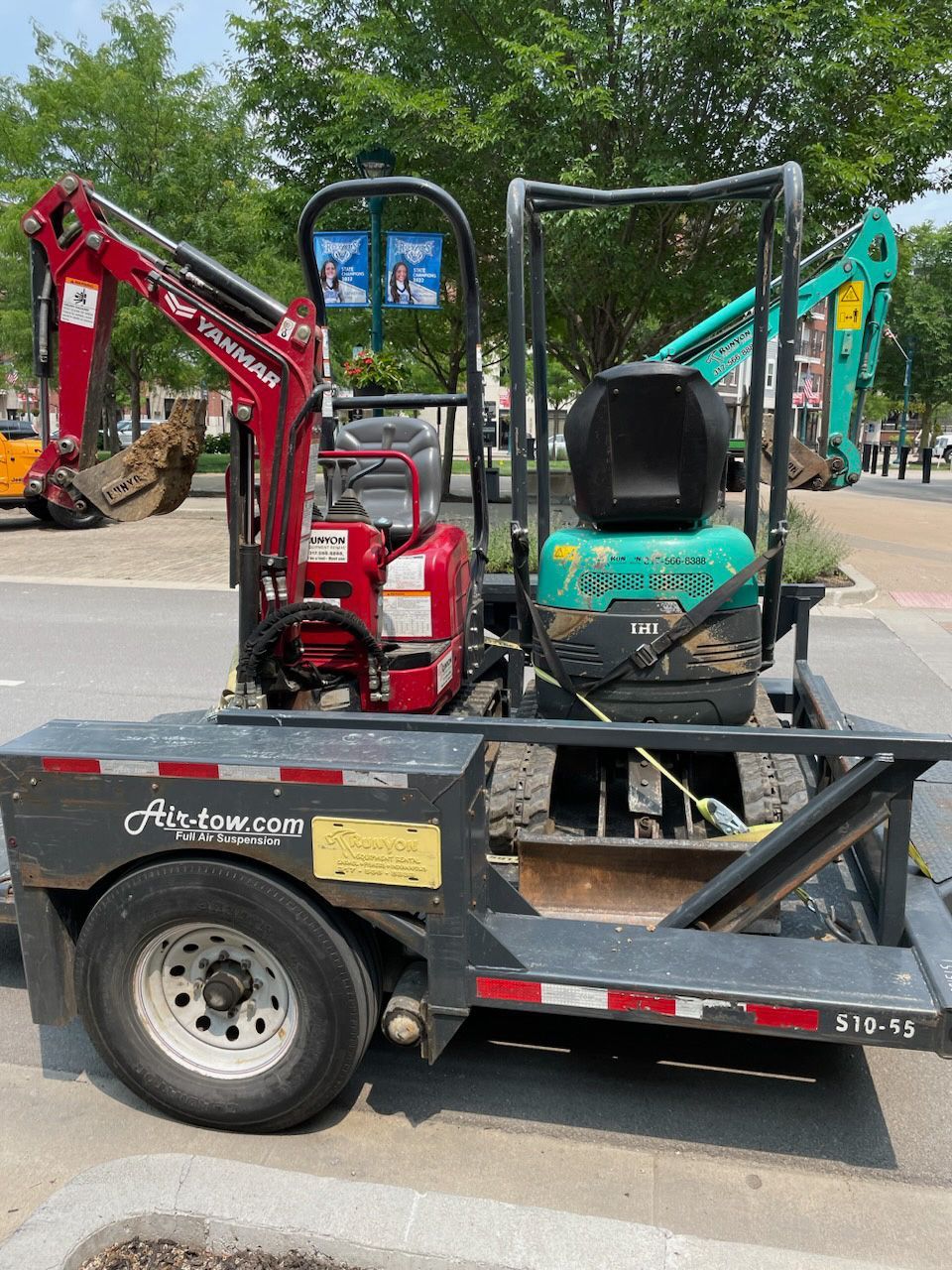 Two small excavators on a trailer; red and teal. Outdoors.