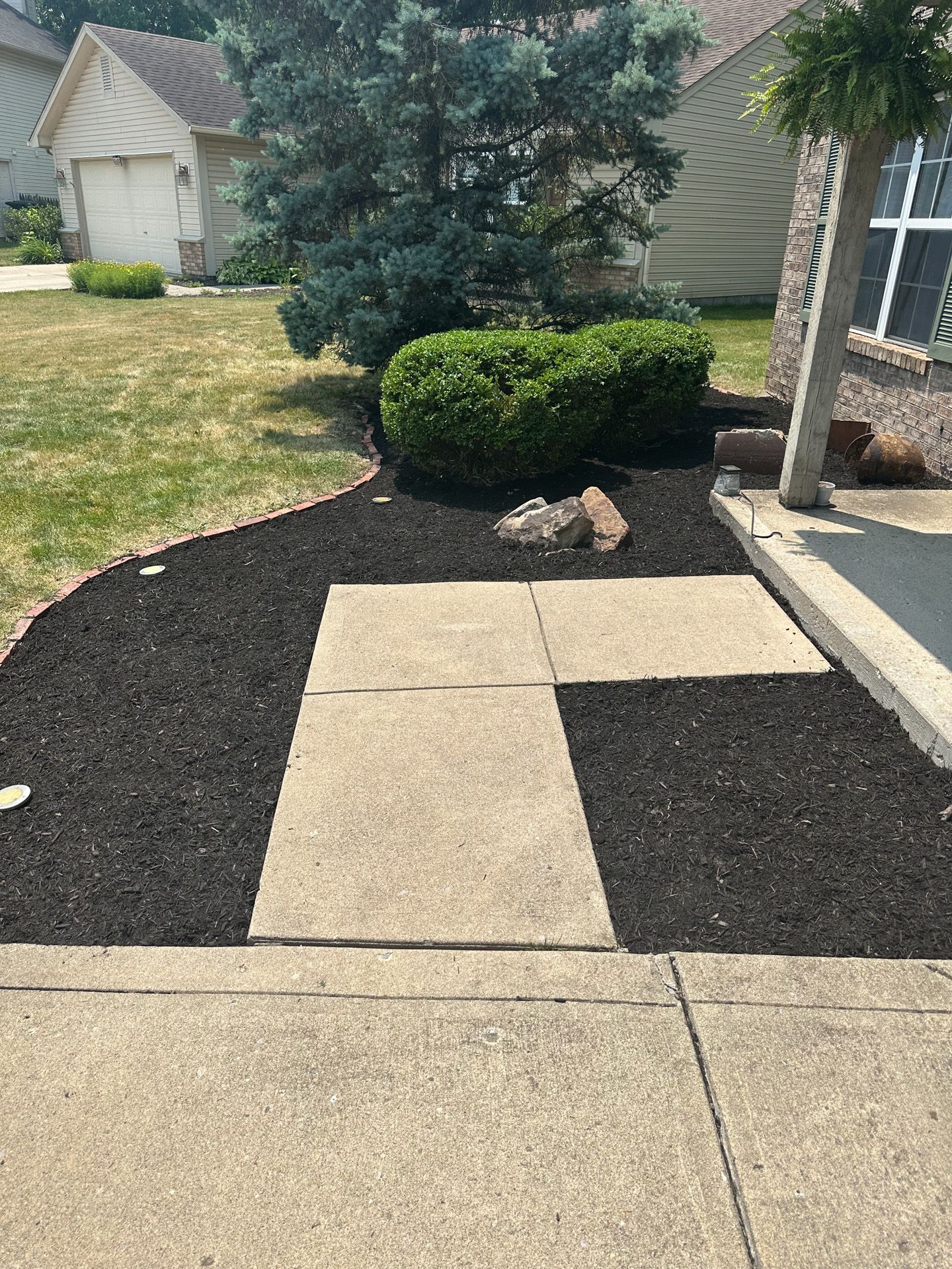 A concrete walkway leads to a house entrance surrounded by black mulch and landscaping.