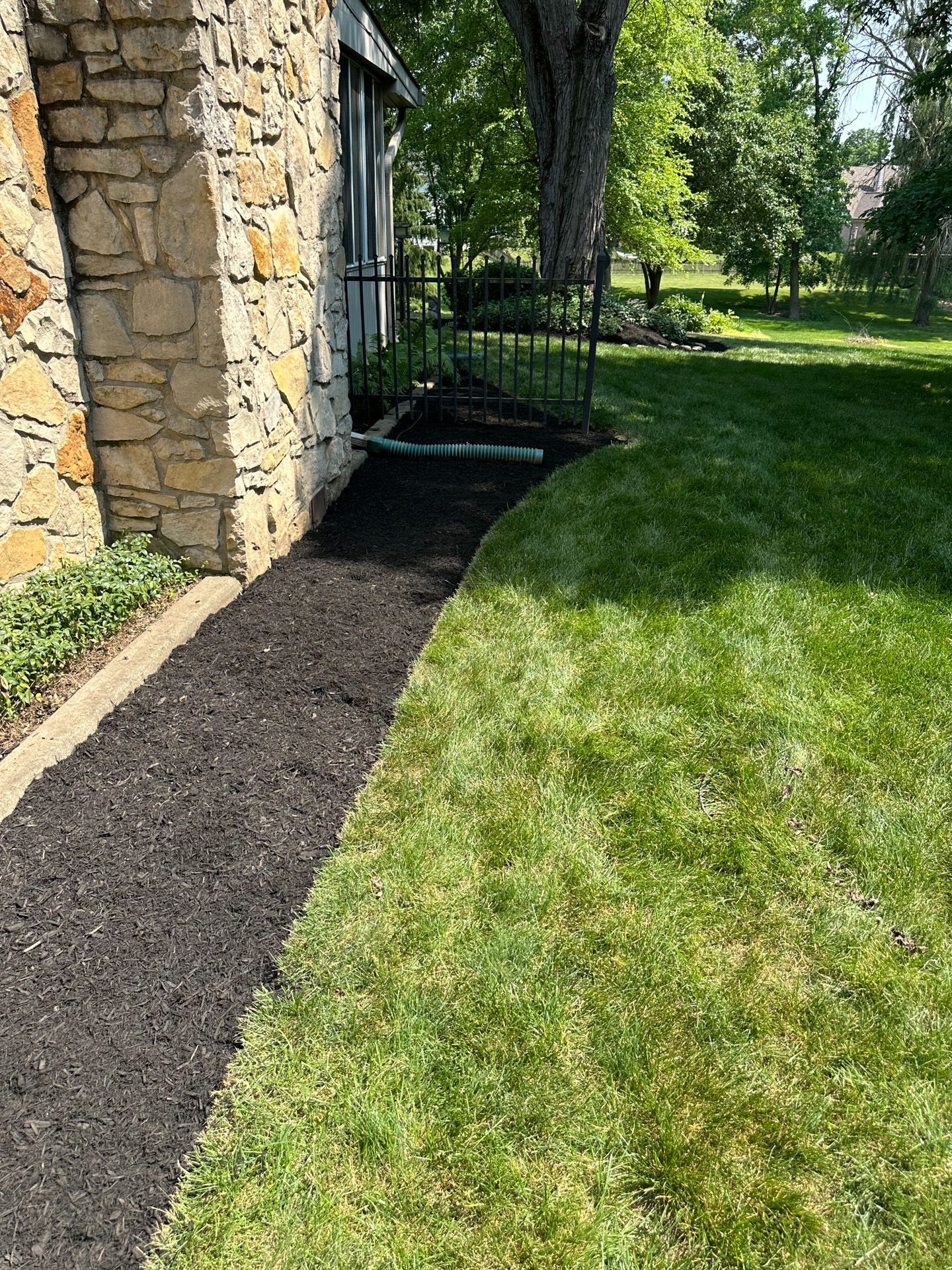 Black mulch pathway alongside green lawn and stone wall.