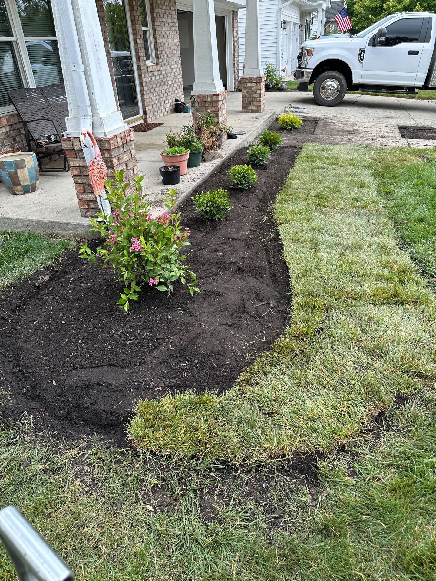 A freshly mulched garden bed with plants and grass next to a house.