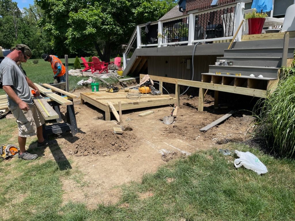 Two people building a wooden deck outdoors on a sunny day.